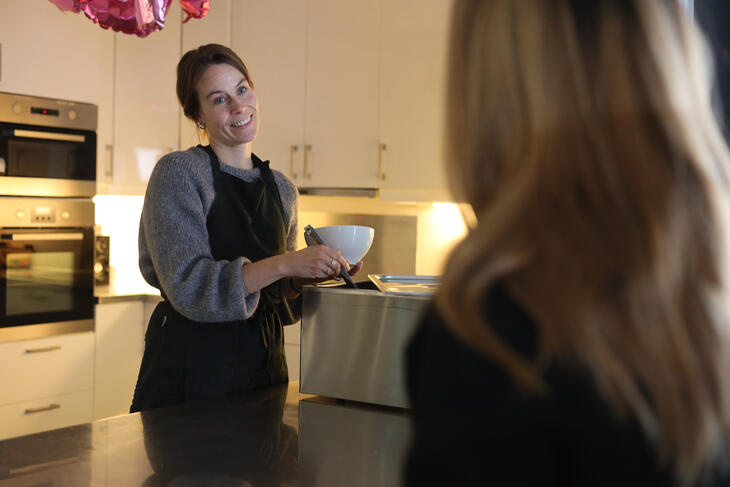 Bilde av en sosialkonsulent som smiler og serverer middag til en bruker i stua. Bilde av en sosialkonsulent som smiler og serverer middag til en bruker i stua.