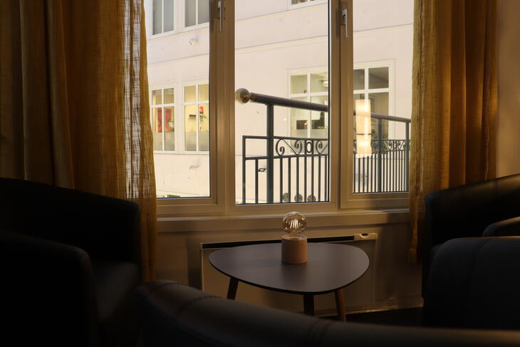 Bilde av et lite bord og stoler foran et vindu i stua. Utenfor vinduet er et balkongrekkverk. Bilde av et lite bord og stoler foran et vindu i stua. Utenfor vinduet er et balkongrekkverk.