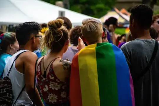Fire personer på Oslo pride sett bakfra. En av dem har et pride flagg over skuldrene.