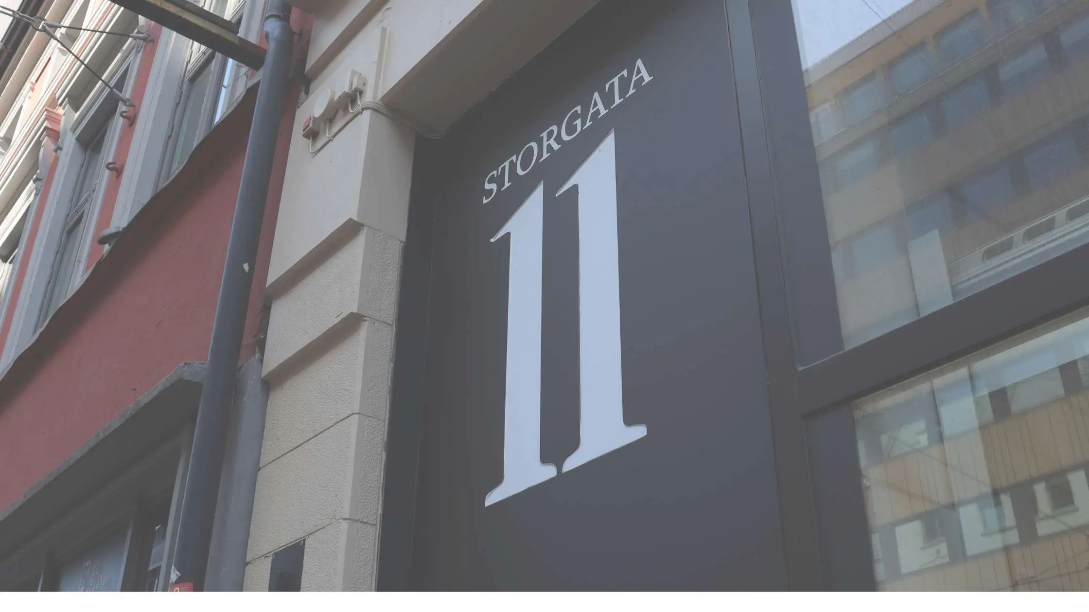 Bilde av et stort nummerskilt med tallet 11, som henger over inngangsdøra i Storgata.