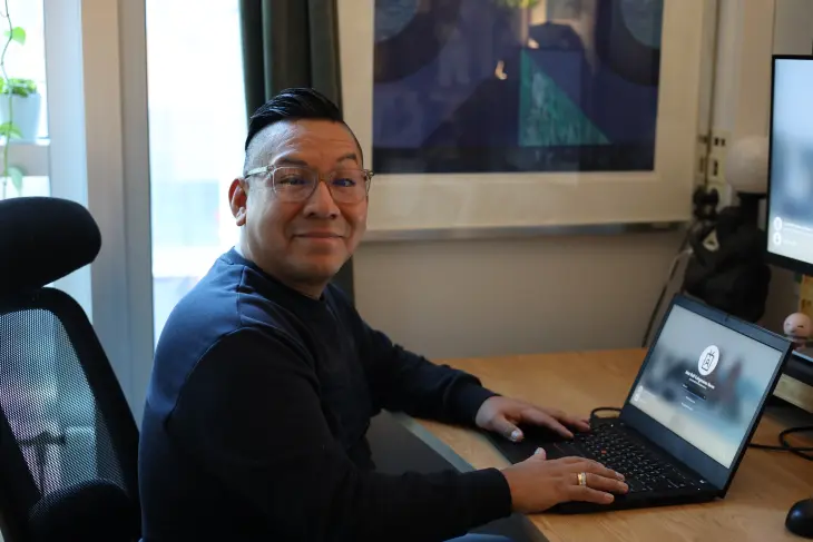 En ansatt på Pro Sentret smiler til kamera mens han sitter på dataen.